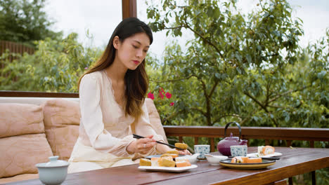 Mujer-Asiática-Comiendo-Sushi-Mientras-Habla-Con-Su-Pareja-Sentada-En-El-Porche-De-Un-Jardín-Japonés