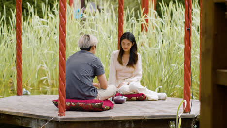 Rückansicht-Eines-Mannes,-Der-Mit-Einer-Japanerin-Auf-Einer-Veranda-In-Einem-Japanischen-Garten-Spricht,-Während-Sie-Tee-Trinken