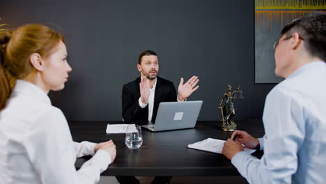 Caucasian-legal-advisor-sitting-at-a-table-with-laptop-in-the-office.-He-is-advising-a-couple