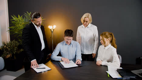 Group-of-multiethnic-legal-advisors-talking-and-reading-documents-at-a-table-in-the-office.-Two-of-them-are-standing-between-two-co-workers