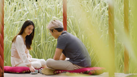 Distant-view-of-a-couple-having-tea-and-talking-while-they-are-sitting-on-cushions-in-a-japanese-garden-porch