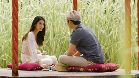 Distant-view-of-a-couple-having-tea-and-talking-while-they-are-sitting-on-cushions-in-a-japanese-garden-porch