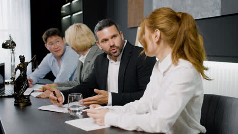 Close-up-view-of-group-of-multiethnic-legal-advisors-talking-and-reading-documents-sitting-at-a-table-in-the-office