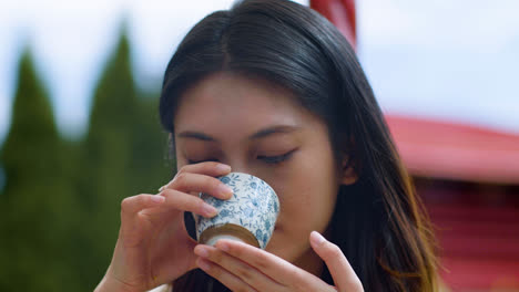 Close-up-view-of-japanese-woman-with-long-hair-drinking-tea-from-a-cup-in-a-japanese-garden