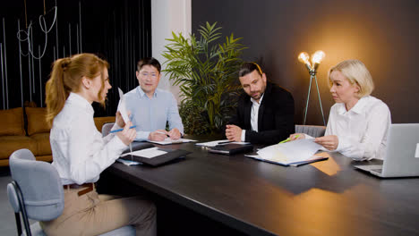 Group-of-multiethnic-legal-advisors-talking-and-reading-documents-sitting-at-a-table-in-the-office