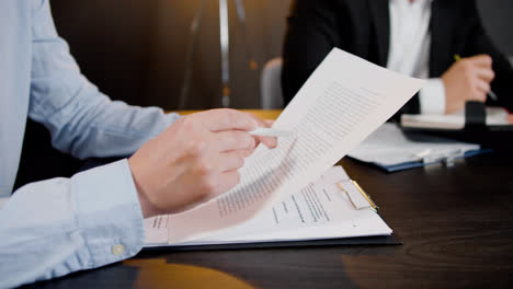 Close-up-view-of-the-hands-of-caucasian-man-holding-pencil-and-reading-a-document-at-a-table