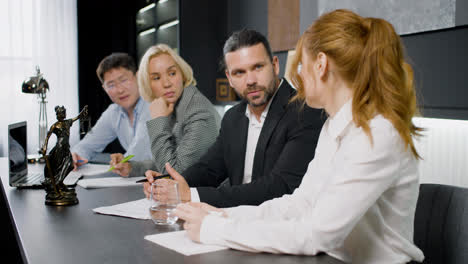 Close-up-view-of-group-of-multiethnic-legal-advisors-talking-and-reading-documents-sitting-at-a-table-in-the-office