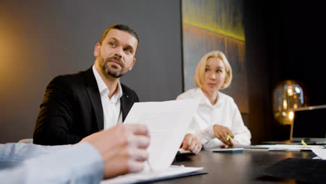 Close-up-view-of-caucasian-legal-advisors-talking-and-reading-documents-with-their-coworkers-sitting-at-a-table-in-the-office