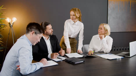 Camera-view-around-of-group-of-multiethnic-legal-advisors-talking-and-reading-documents-sitting-at-a-table-in-the-office.-One-of-them-is-standing-between-two-co-workers