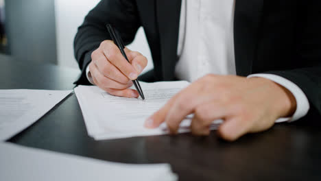 Close-up-view-of-the-hands-of-caucasian-man-writing-on-a-document-at-the-table-in-the-office.-His-costumer-is-making-gestures-to-explain-something-to-him