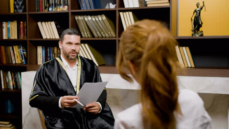 Caucasian-male-legal-advisor-wearing-toga-and-sitting-on-a-chair-in-the-office.-He-is-advising-a-client