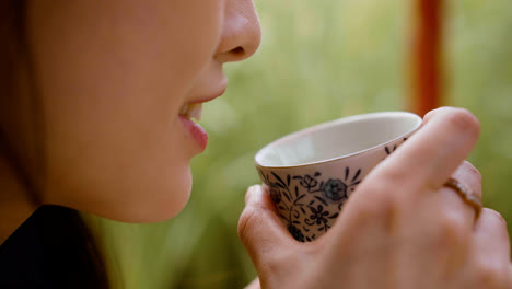 Close-up-view-of-japanese-woman-with-long-hair-drinking-tea-from-a-cup-in-a-japanese-garden