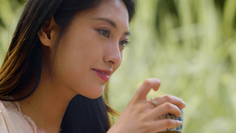 Close-up-view-of-japanese-woman-with-long-hair-drinking-tea-from-a-cup-in-a-japanese-garden