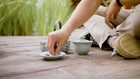 Vista-De-Cerca-De-La-Mano-De-Un-Hombre-Japonés-Sentado-En-Un-Jardín-Japonés,-Preparando-Té-Y-Vertiéndolo-En-Tazas.