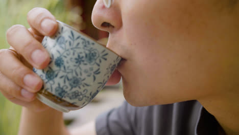 Close-up-view-of-japanese-man-in-glasses-drinking-tea-from-a-cup-in-a-japanese-garden