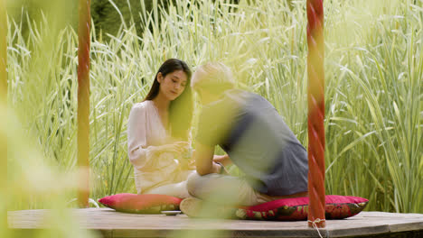 Distant-view-of-a-couple-having-tea-and-talking-while-they-are-sitting-on-cushions-in-a-japanese-garden-porch