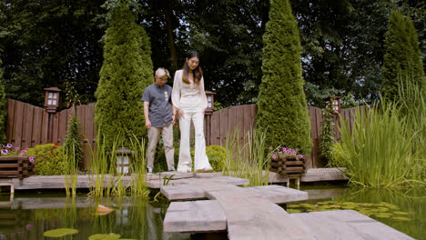 Japanese-couple-walking-over-the-bridge-of-a-Japanese-garden.-They-stop-on-the-porch