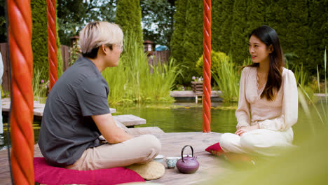 Japanese-couple-sitting-on-cushions-on-a-japanese-garden-porch-having-tea-and-talking