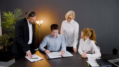 Asian-man-signing-a-document-sitting-at-table-in-the-office-while-legal-advisors-supervise