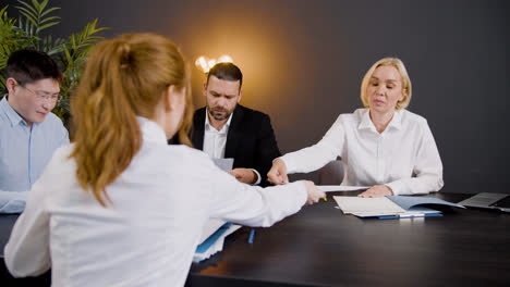 Camera-view-around-of-group-of-multiethnic-legal-advisors-talking-and-reading-documents-sitting-at-a-table-in-the-office