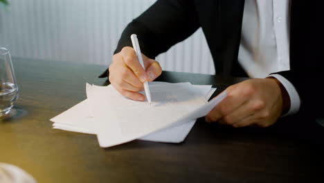 Close-up-view-of-the-hands-of-caucasian-man-holding-pencil-and-reading-a-document-at-a-table.-Then-he-gives-the-document-to-a-woman