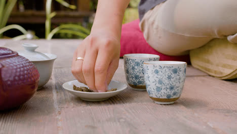 Vista-De-Cerca-De-Las-Manos-De-Un-Hombre-Japonés-Sentado-En-Un-Jardín-Japonés,-Preparando-Té-Y-Vertiéndolo-En-Tazas.