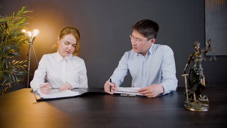 Front-view-of-multiethnic-legal-advisors-talking-and-reading-documents-at-a-table-in-the-office