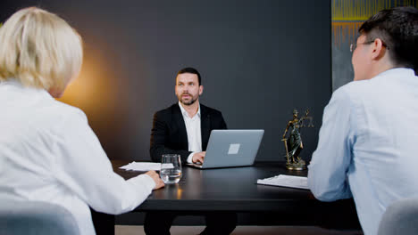 Caucasian-legal-advisor-sitting-at-a-table-with-laptop-in-the-office.-He-is-advising-a-couple