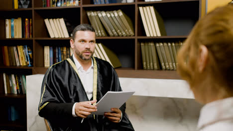 Camera-zoom-out-on-caucasian-male-legal-advisor-wearing-toga-and-sitting-on-a-chair-in-the-office.-He-is-advising-a-client