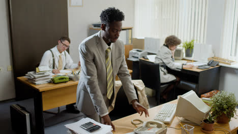 African-american-businessman-working-stading-near-his-desk-and-talking-on-the-phone-in-a-vintage-office.