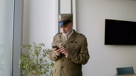 Old-man-using-smartphone-and-looking-out-of-the-window