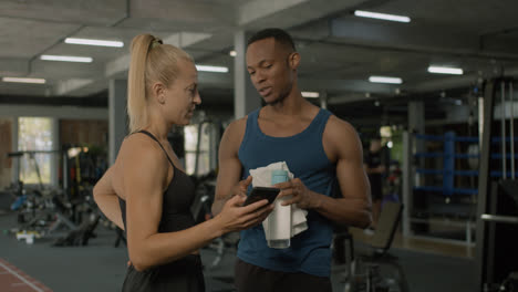 Caucasian-female-monitor-and-an-athletic-african-american-man-talking-in-the-gym.