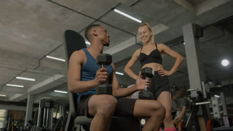Lower-view-of-caucasian-female-monitor-and-an-athletic-african-american-man-talking-in-the-gym.