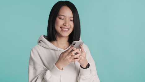 Asian-woman-texting-on-smartphone-and-laughing-on-camera.
