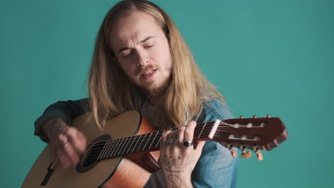Caucasian-young-man-playing-guitar-and-singing-on-camera.