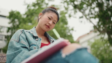 Asiatische-Frau-Schreibt-Im-Park-In-Ein-Notizbuch.