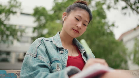 Asiatische-Frau-Schreibt-Im-Park-In-Ein-Notizbuch.