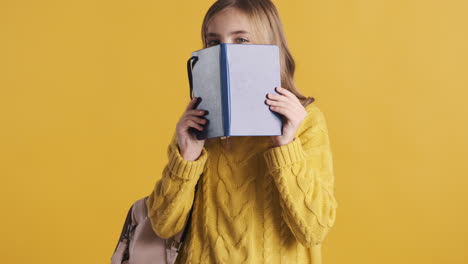 Happy-teenage-Caucasian-girl-student-holding-notebook-in-front-of-her-head.