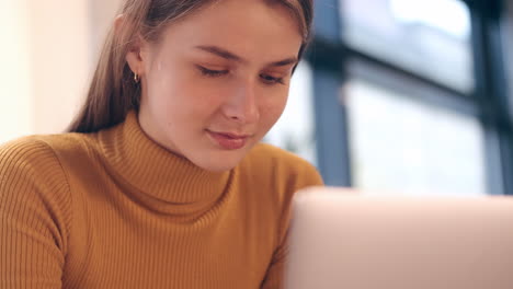 Close-up-shot-of-Caucasian-smiling-student-girl-dreamily-working-on-laptop-in-cafe.