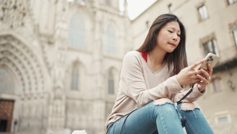 Asiatisches-Mädchen-Testet-Auf-Ihrem-Smartphone-Und-Wartet-Draußen-Auf-Einen-Freund.