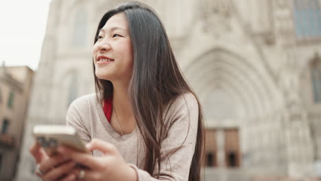 Chica-Asiática-Enviando-Mensajes-De-Texto-En-Un-Teléfono-Inteligente-Al-Aire-Libre.