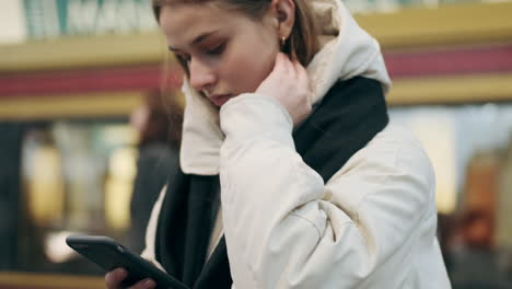 Caucasian-teenager-girl-in-down-jacket-with-scarf-thoughtfully-using-cellphone-outdoor.