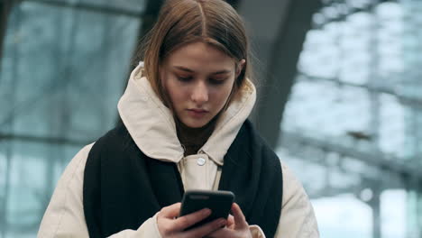 Caucasian-teenage-girl-in-down-jacket-with-scarf-intently-using-cellphone-at-subway-station.