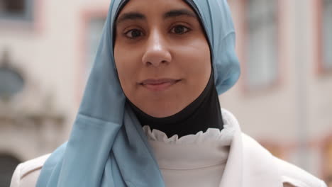 Portrait-of-young-Arabian-woman-dreamily-looking-in-camera-and-smiling-on-city-street.