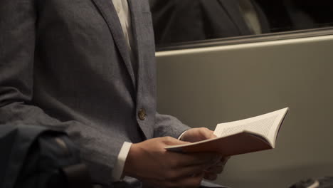 Close-up-shot-of-businessman-in-suit-reading-book-in-subway-train-on-the-subway.