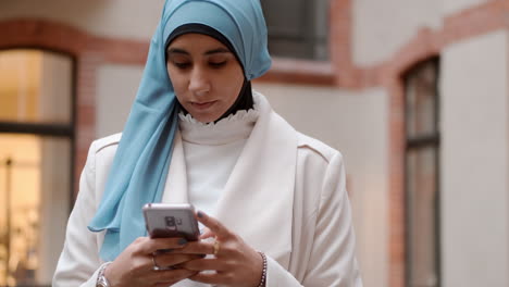 Mujer-árabe-Joven-Usando-Con-Confianza-Su-Teléfono-Celular-En-La-Calle-De-La-Ciudad.