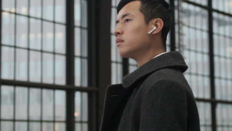 Young-Asian-man-with-wireless-earphones-confidently-waiting-train-at-subway-station.