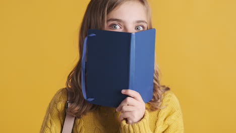 Happy-teenage-Caucasian-girl-student-holding-notebook-in-front-of-her-head.