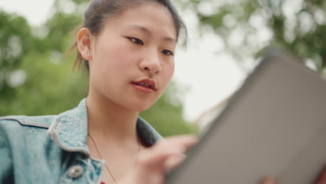 Asiatisches-Mädchen-Sitzt-Im-Park-Und-Scrollt-Auf-Ihrem-Tablet-Gerät.