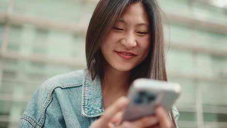 Mujer-Asiática-Sonriendo-Y-Mirando-Su-Teléfono-Al-Aire-Libre.